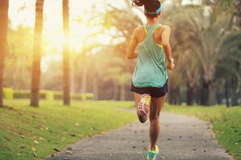 Healthy young sporty woman running on a park trail at sunrise.
